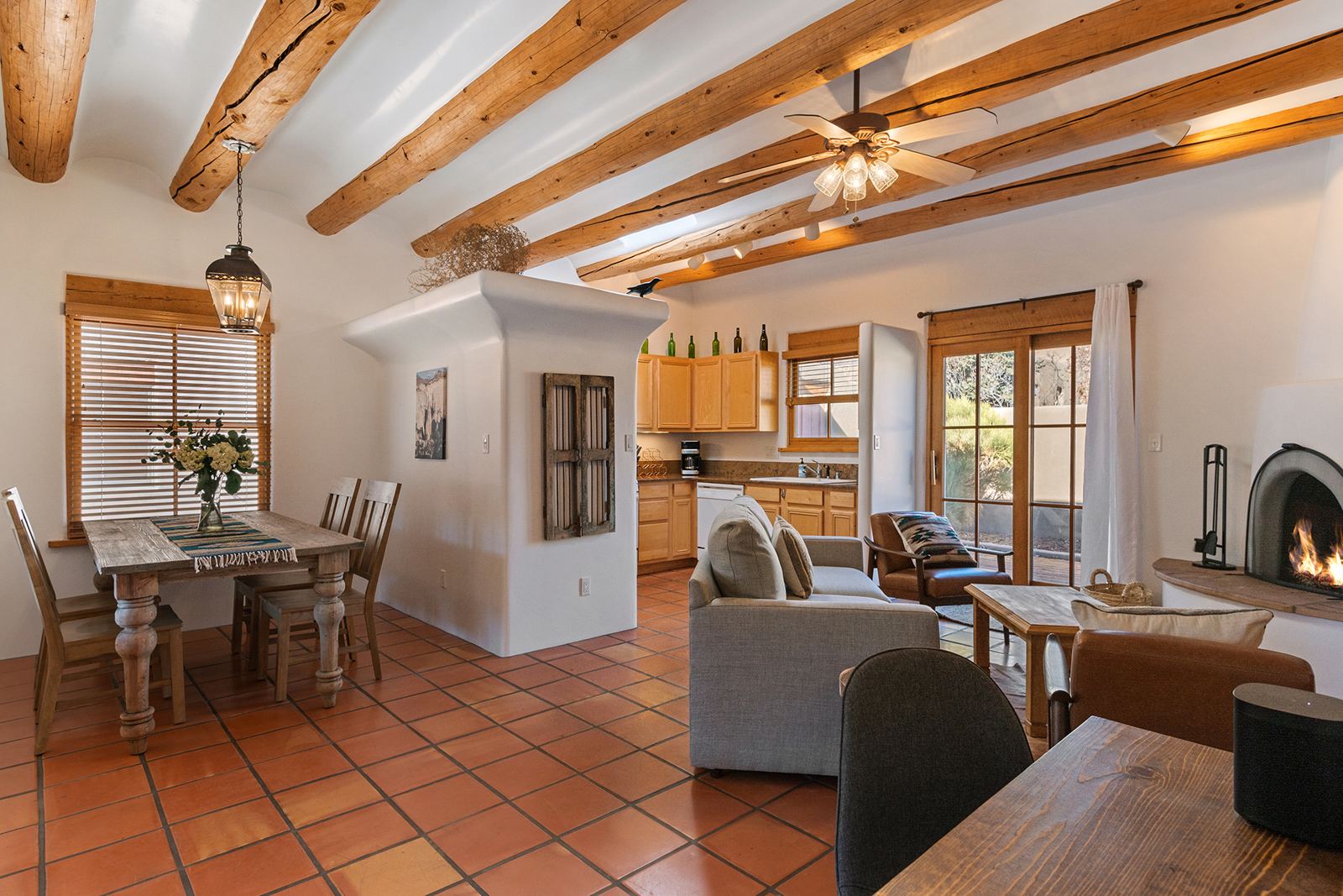 Open living, dining and kitchen under vigas, with saltillo tile floors